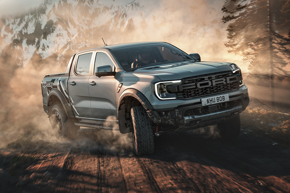Un Ford Ranger Raptor in modalità Baja percorre una strada sterrata con un paesaggio montano sullo sfondo.