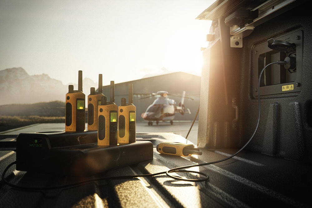 Diversi walkie-talkie in carica nel pianale di un Ranger Raptor al tramonto, con un elicottero in lontananza.