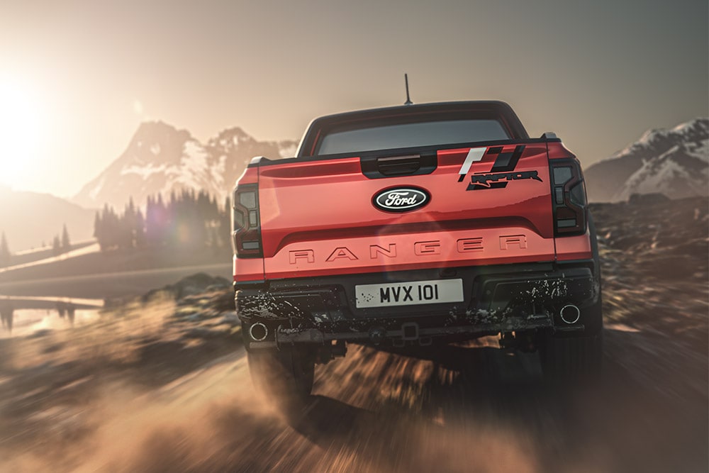 Vista posteriore di un Ford Ranger Raptor rosso che percorre una strada sterrata con montagne sullo sfondo.