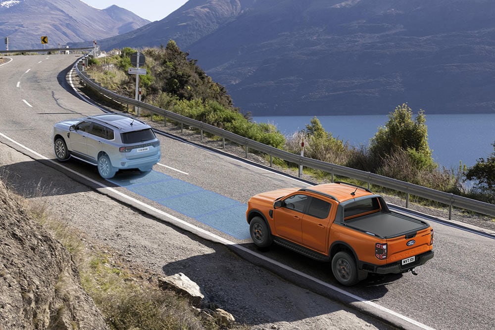 Un Ford Ranger Raptor giallo percorre una strada panoramica di montagna, con dettaglio dei sistemi di assistenza alla guida del veicolo.