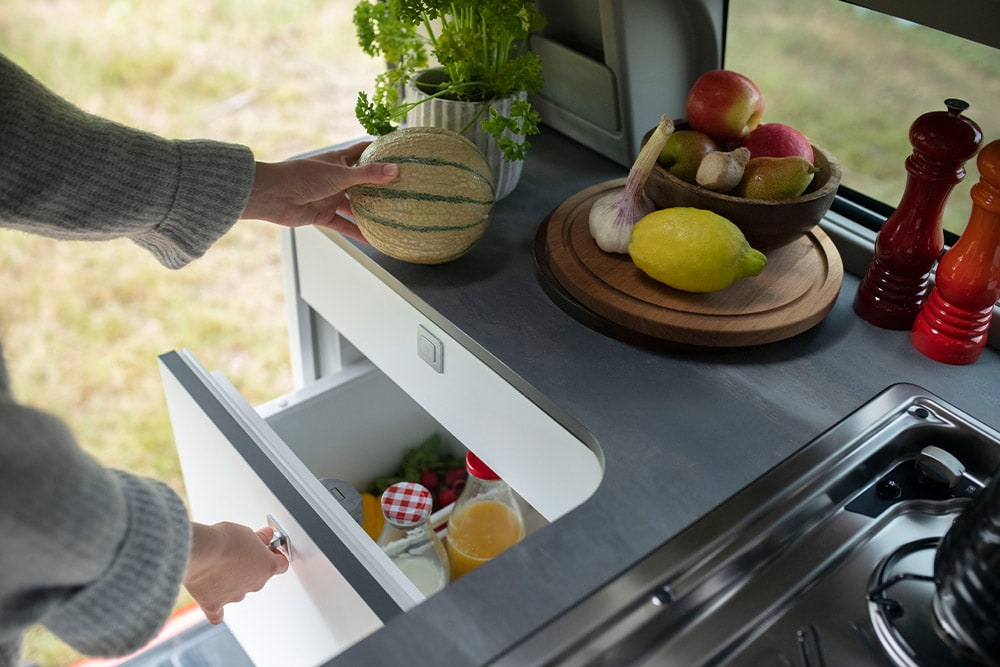 Frigorifero a cassetto da 33 litri integrato nel Ford Transit Custom Nugget con frutta sul piano di lavoro.