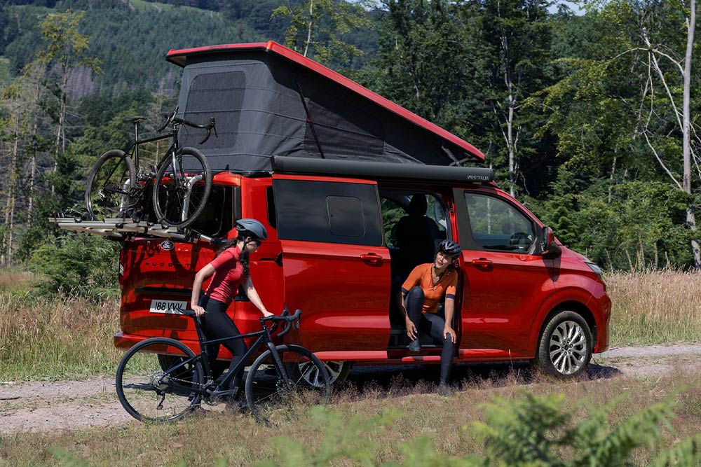 Persone che scaricano biciclette dal portabici di un Ford Transit Custom Nugget rosso.