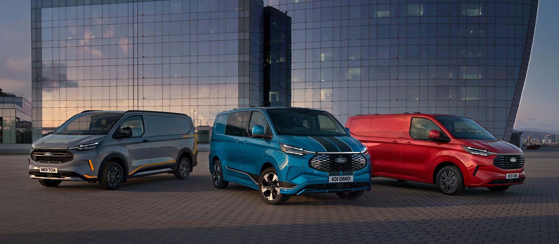 Tre furgoni Ford Transit Custom Sport in grigio, blu e rosso parcheggiati. 