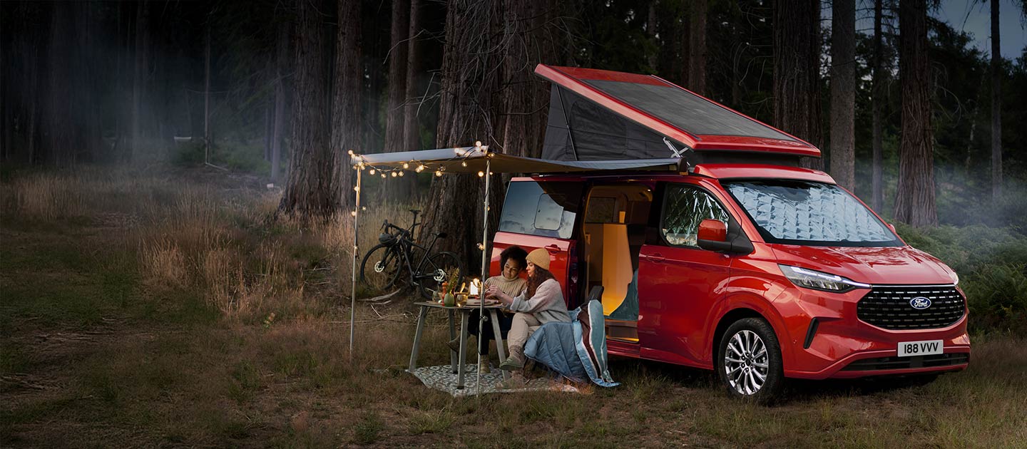 Un camper Ford Transit Custom Nugget rosso parcheggiato in un bosco.