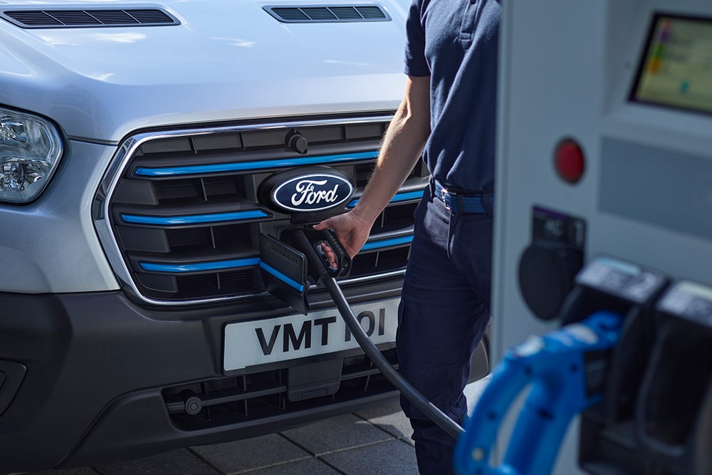 Primo piano di una persona che collega un cavo di ricarica a un furgone elettrico Ford E-Transit versione argento.
