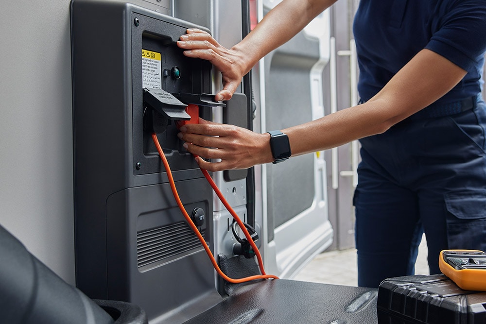 Primo piano di una persona che collega un cavo di ricarica all'interno di un furgone elettrico Ford E-Transit .