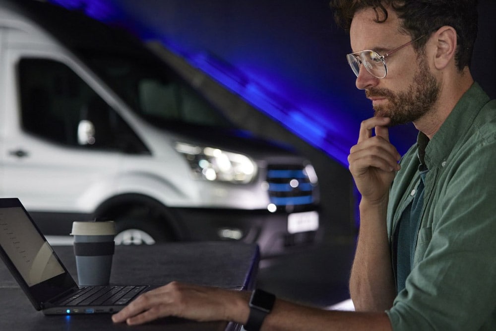 Un uomo che lavora con un PC portatile e un furgone elettrico Ford E-Transit  sullo sfondo.