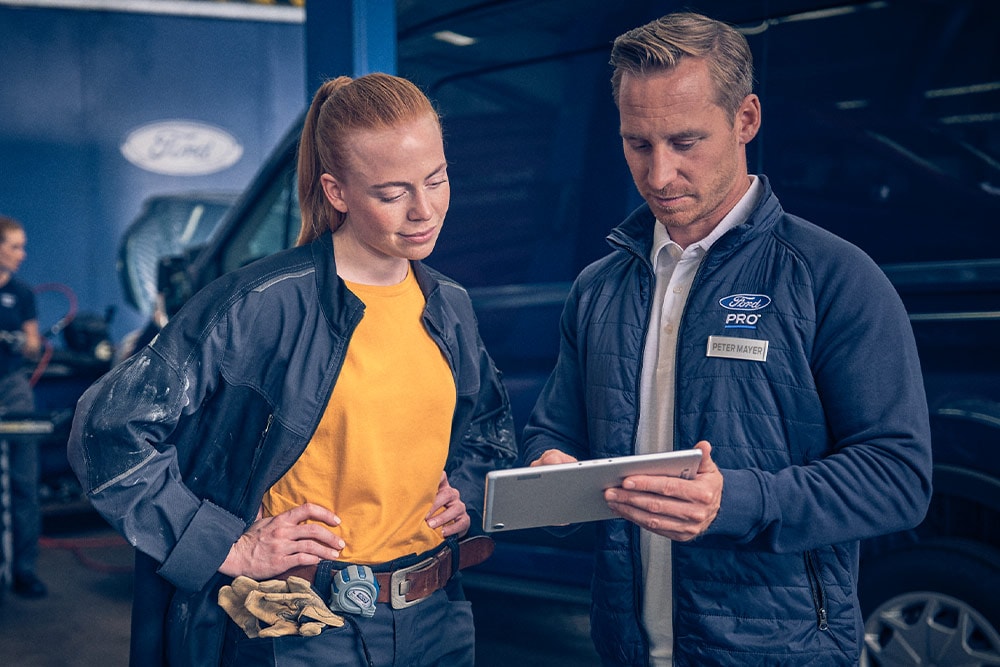 Due meccanici in un'officina che guardano un tablet di fronte a un furgone elettrico Ford E-Transit .