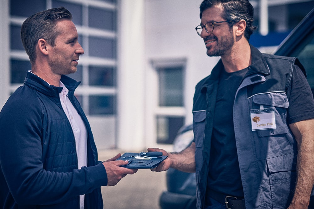 Un uomo consegna un tablet a un altro uomo di fronte a un furgone Ford Transit.