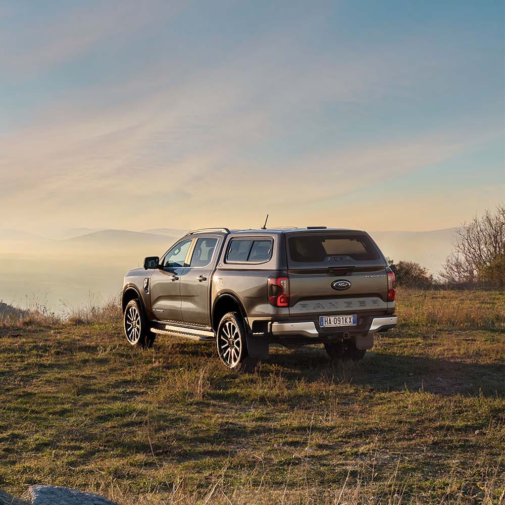 Ford Ranger grigio con cassone coperto su collina erbosa al tramonto.