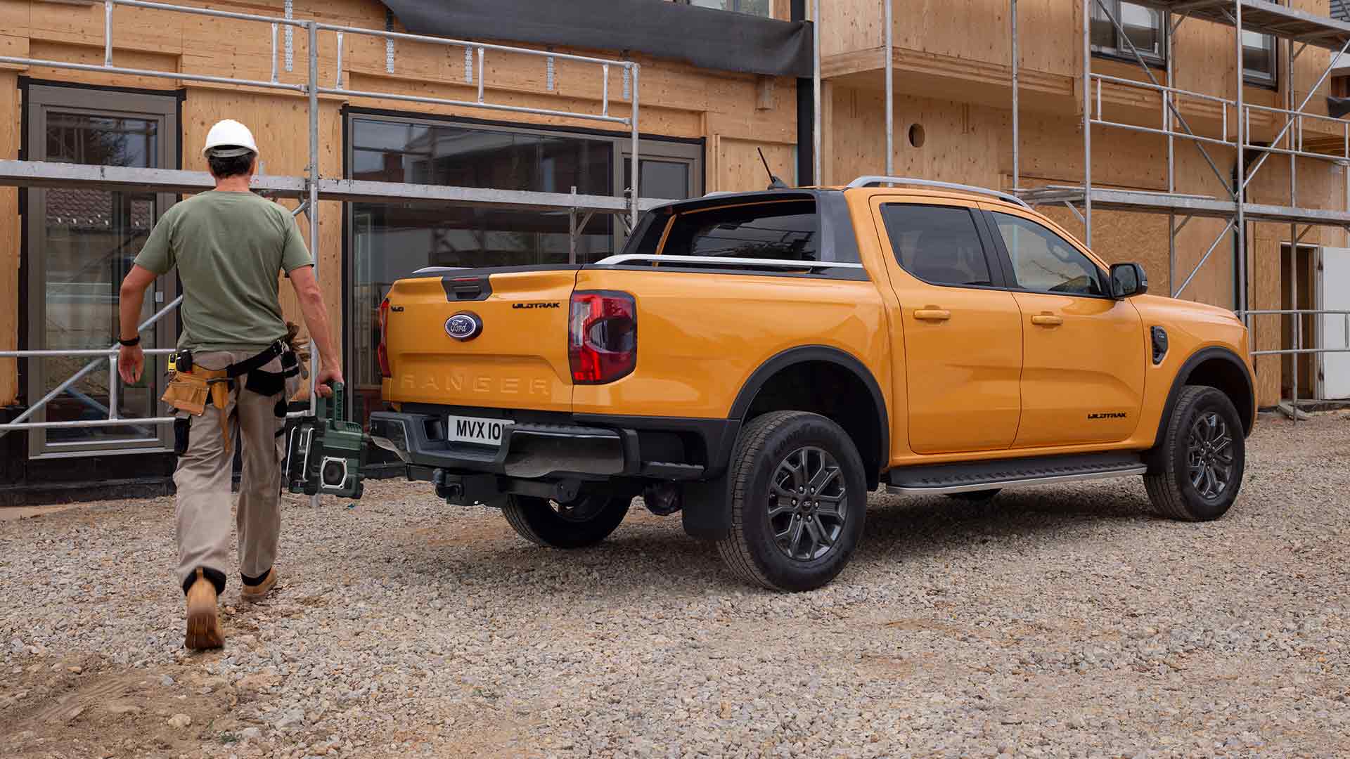 Vista posteriore a tre quarti di un Ford Ranger Wildtrak Doppia Cabina giallo in un cantiere edile.