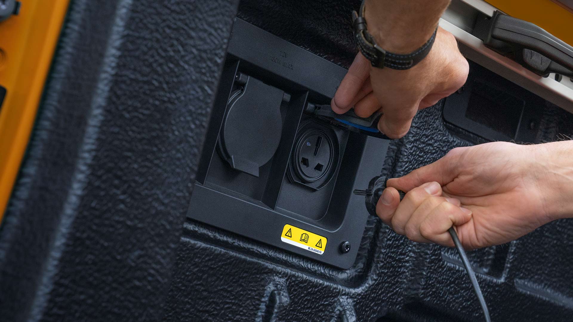 Primo piano delle mani che collegano i cavi alla presa di corrente nel pianale del Ford Ranger.