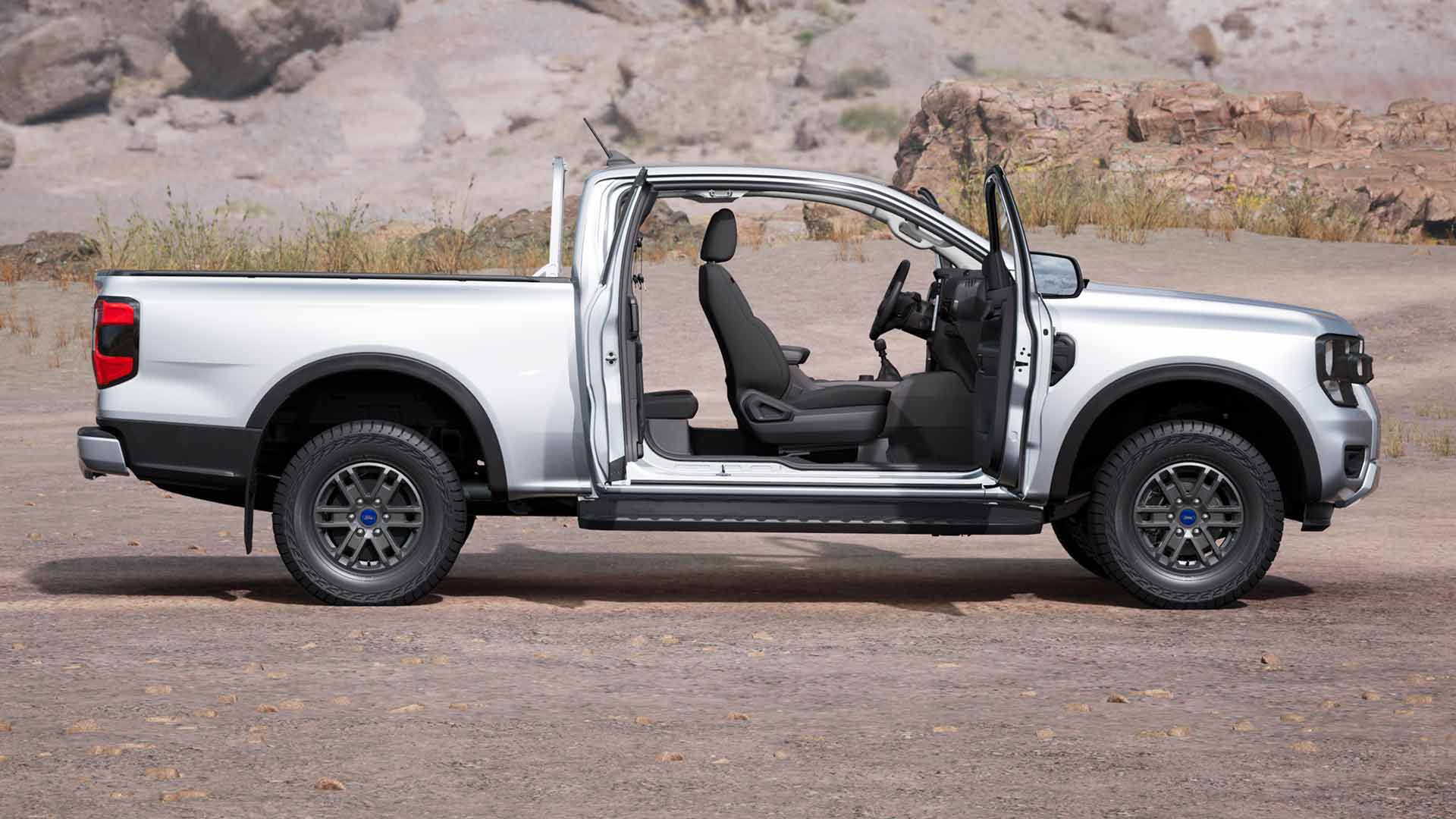 Profilo di un Ford Ranger XLT Super Cab color argento con portiere aperte, parcheggiato in un terreno polveroso.