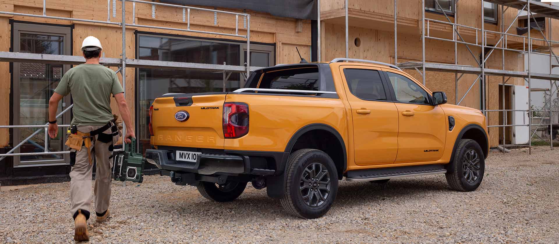 Un operaio con caschetto si dirige verso un pick-up Ford Ranger giallo in un cantiere edile.