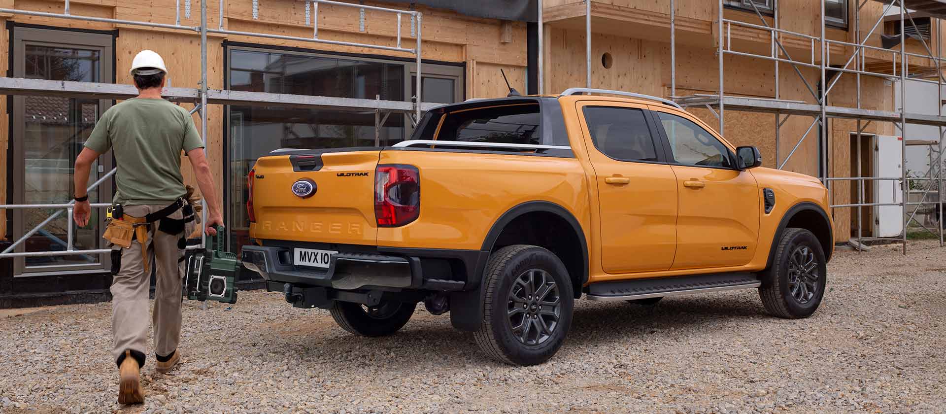 Vista posteriore a tre quarti di un Ford Ranger Wildtrak Doppia Cabina giallo in un cantiere edile.