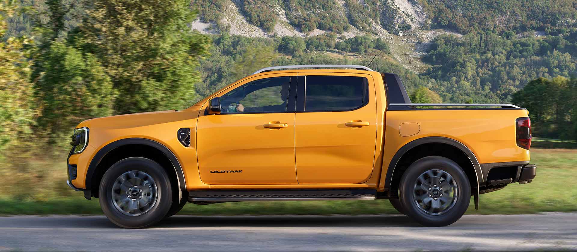 Vista laterale di un Ford Ranger Wildtrak Doppia Cabina giallo parcheggiato sul ciglio di una strada di montagna.