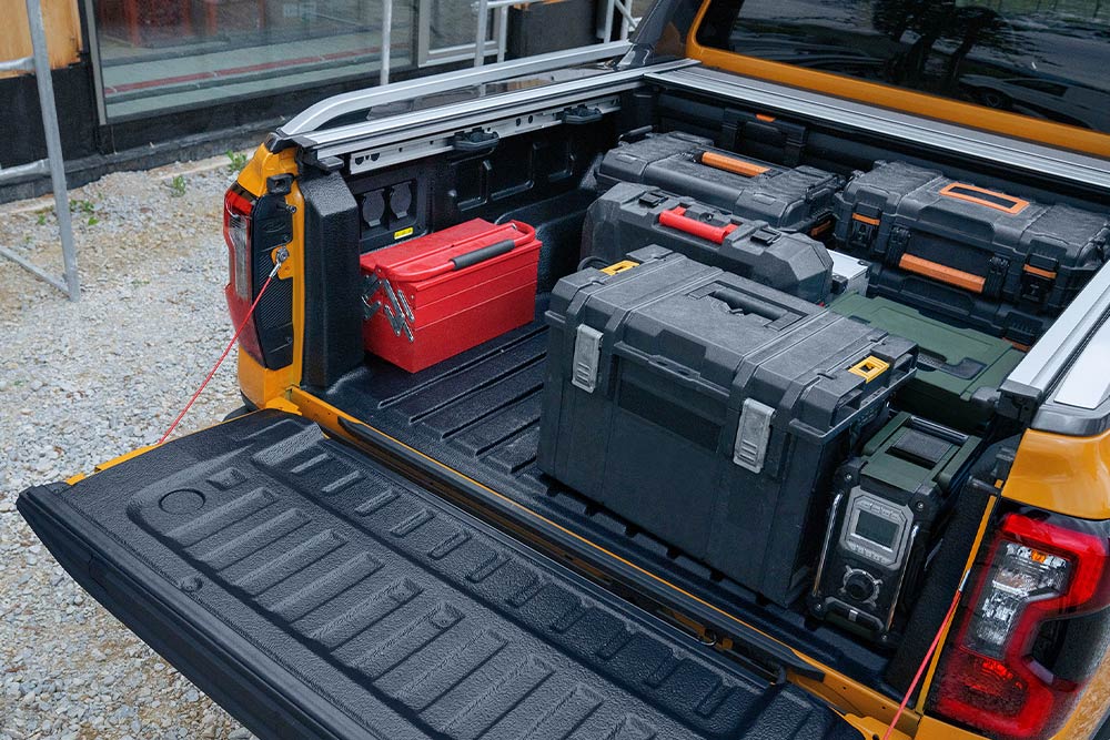 The tailgate of a yellow Ford Ranger is down, with a wooden plank secured to it using clamp.
