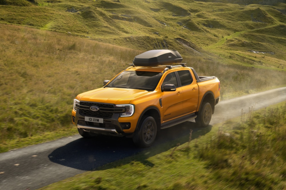 Yellow Ford Ranger driving on a rural road with a roof box mounted on roof cross bars on the roof.