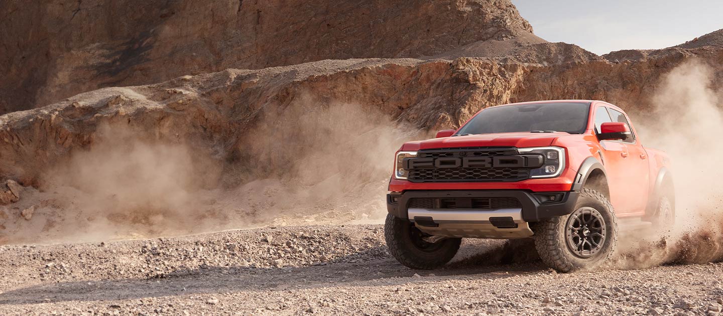 Un Ford Ranger Raptor rosso solleva la polvere mentre attraversa un paesaggio desertico.