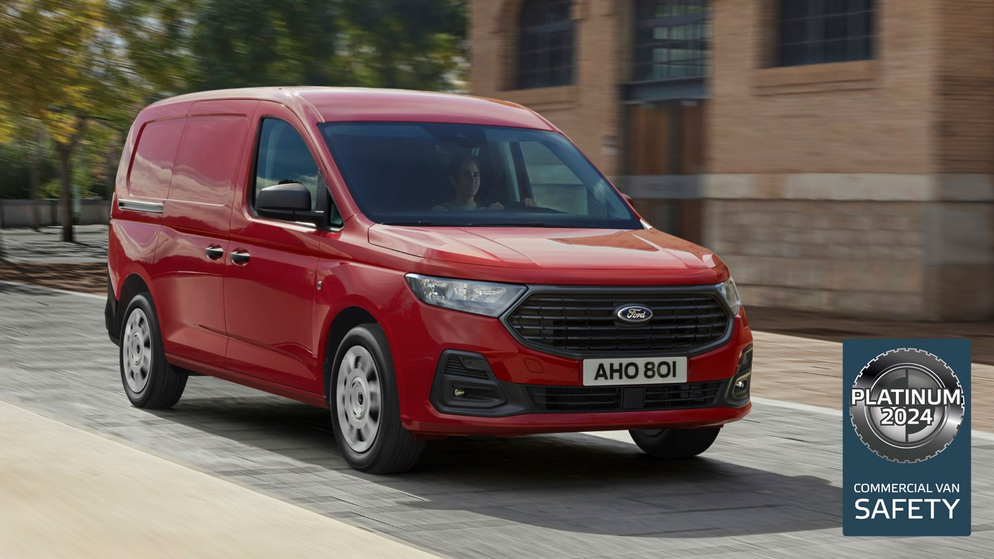 Il nuovo Ford Transit Connect Trend in Maple Red percorre una strada, con la griglia anteriore e i fari automatici in evidenza. 