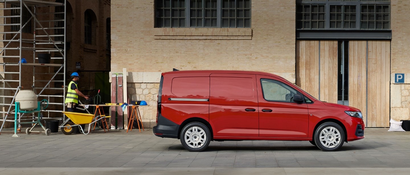 Il nuovo Ford Transit Connect Trend in Maple Red percorre una strada, con la griglia anteriore e i fari automatici in evidenza. 