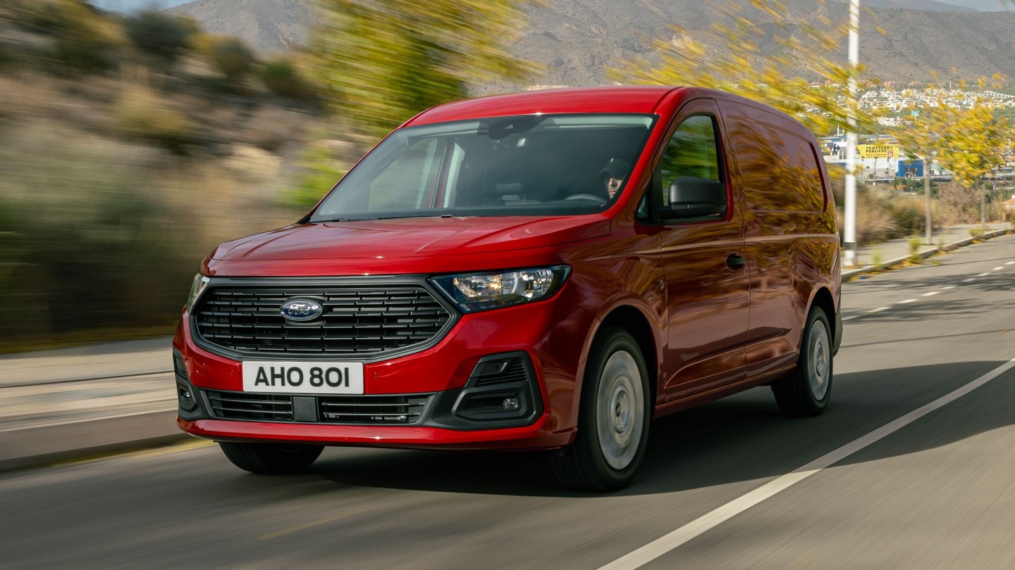 Il nuovo Ford Transit Connect in Maple Red percorre una strada con la griglia anteriore e i fari in evidenza. 
