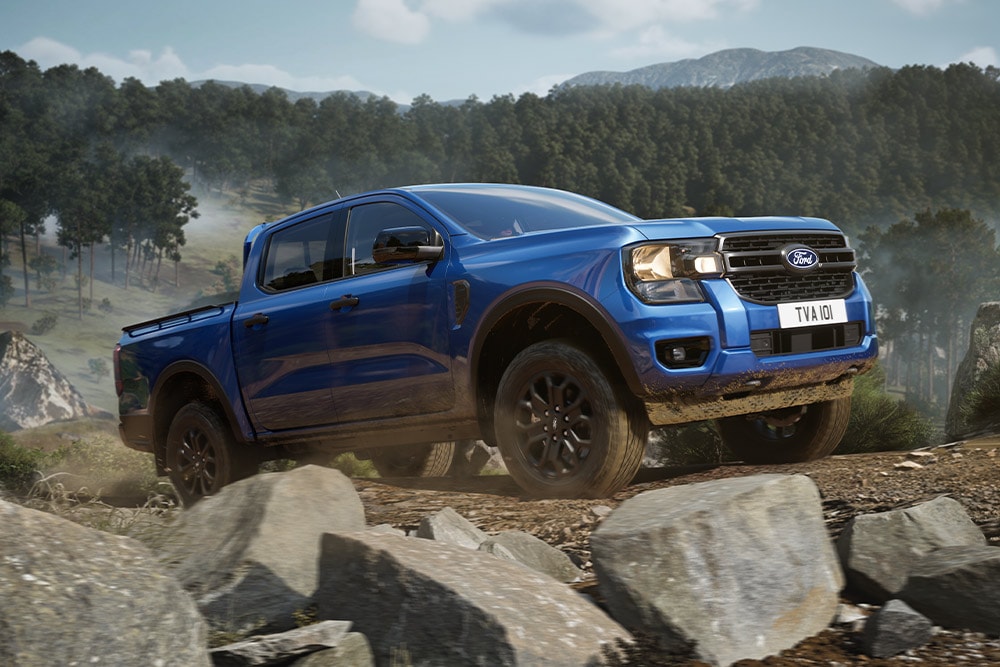 Un pick-up Ford Ranger blu percorre una strada sterrata attraverso una foresta, lasciando una scia di polvere.