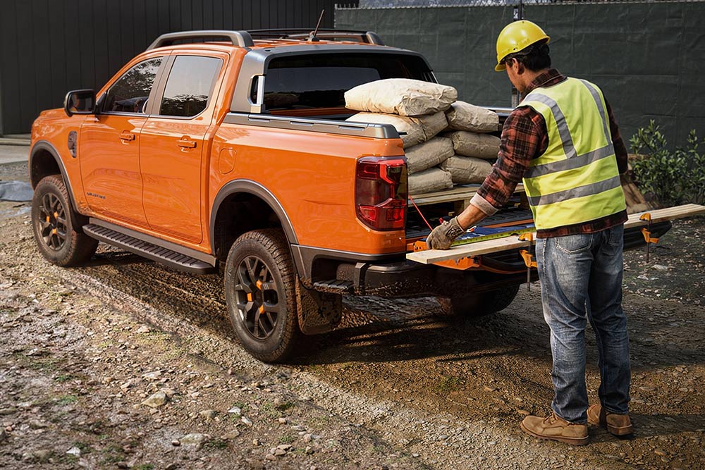Un operaio edile che carica attrezzatura sul pianale di un Ford Ranger arancione.