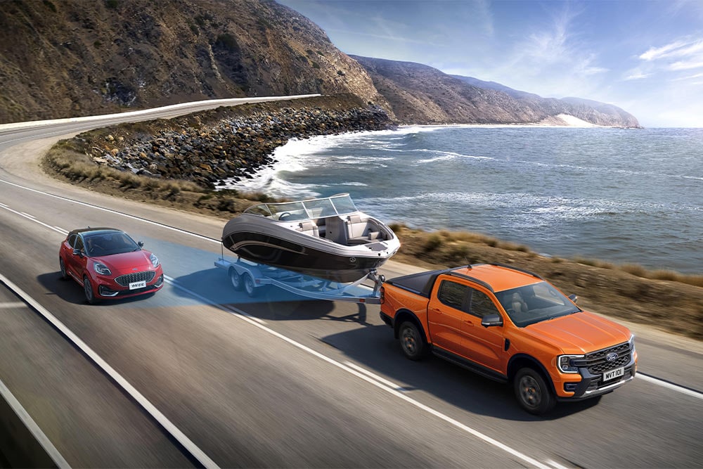 Un Ford Ranger arancione traina una barca lungo una strada costiera, dimostrando la sua capacità di traino.