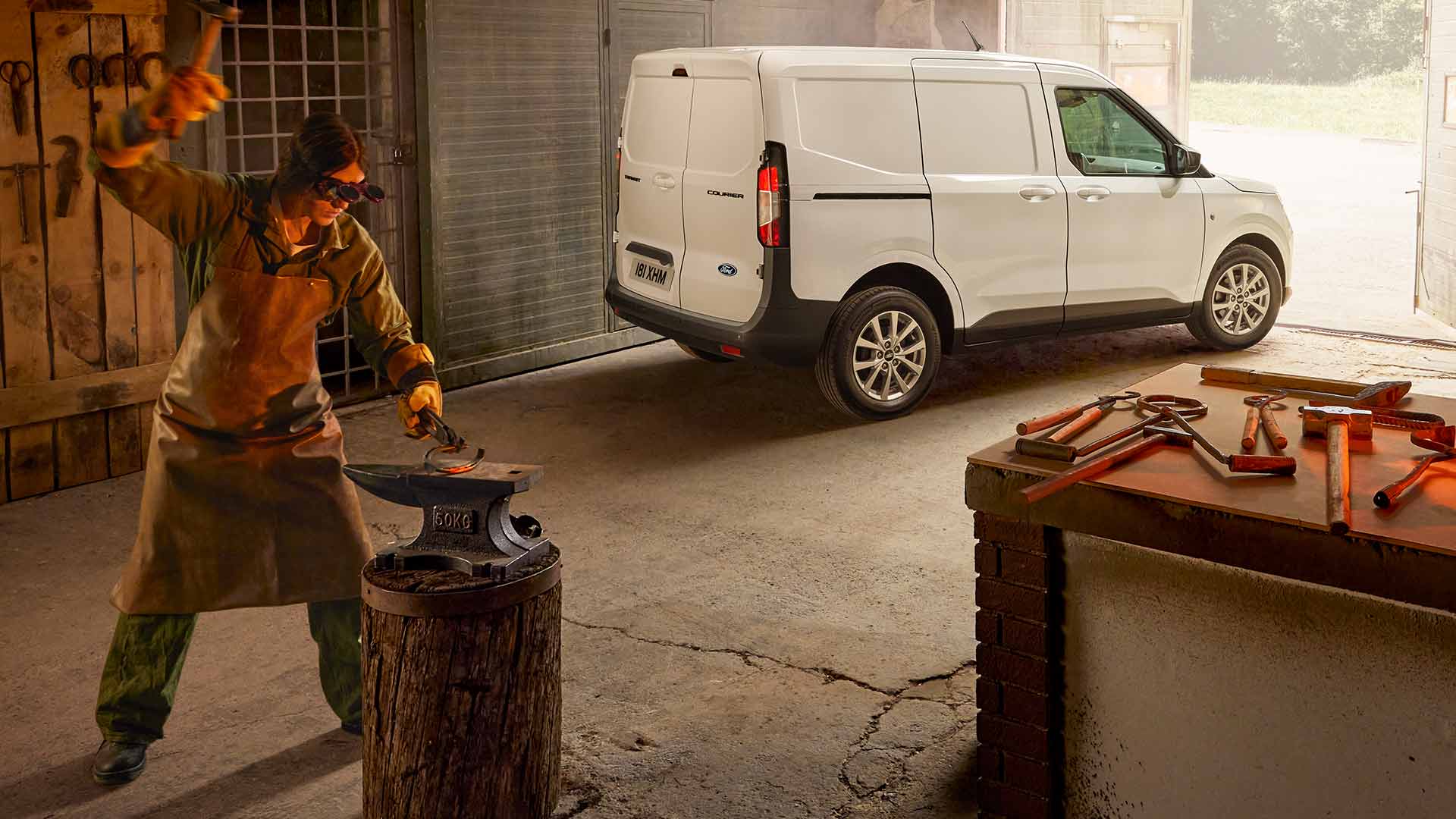 Blacksmith hammering with a White Ford Transit Courier Van in the background 