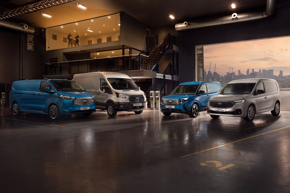 Flotta di Ford Transit in uno showroom con uno skyline cittadino al tramonto sullo sfondo.