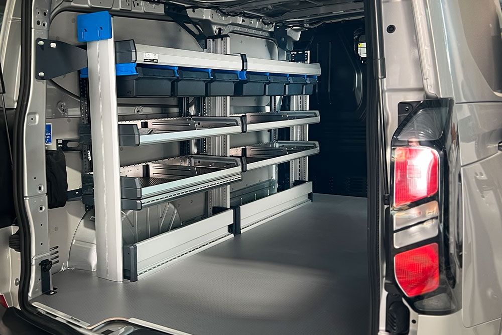 Interno posteriore di un furgone Ford Transit, che mostra un sistema di scaffalature modulari con vari contenitori.