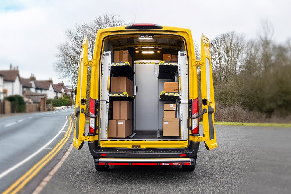 Vista posteriore di un furgone Ford Transit giallo con porte aperte, che rivela un interno organizzato con scaffali e scatole.
