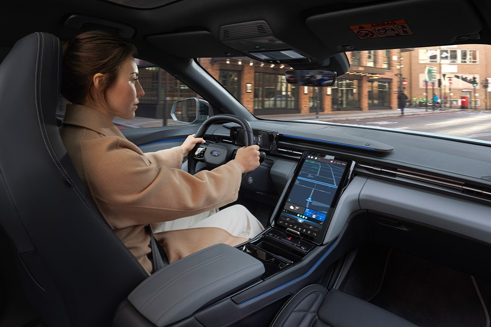 Una persona alla guida di un veicolo Ford, con il sistema di navigazione attivo e visibile sull'ampio touchscreen centrale.