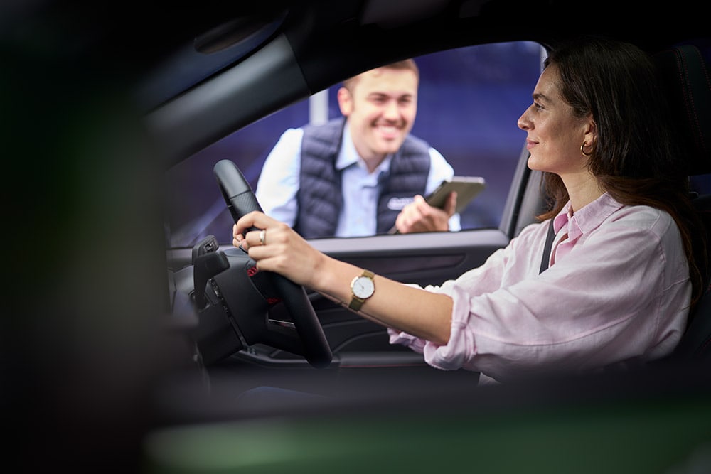 Una persona al posto di guida di un'auto Ford con lo sguardo rivolto verso un tecnico con in mano un tablet, all'esterno dell'abitacolo.