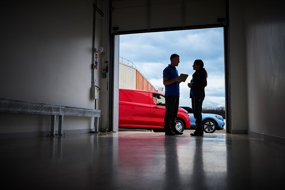 Due persone che parlano sulla soglia di un garage, con un furgone Ford rosso e un SUV Ford blu parcheggiati all'esterno.