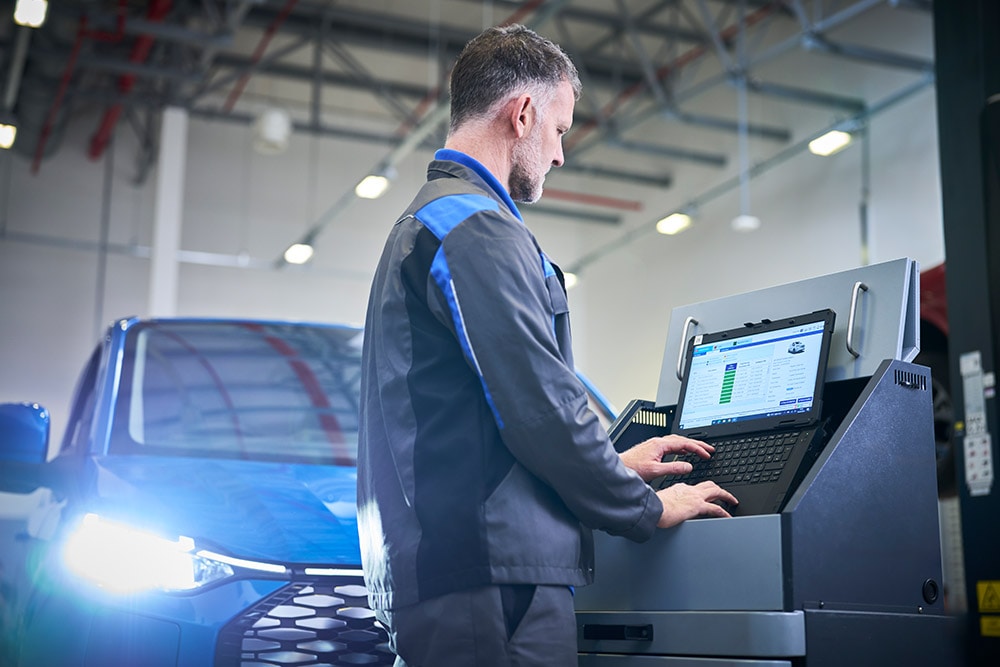 Un tecnico che utilizza un PC collegato a un SUV Ford blu in una postazione di servizio.
