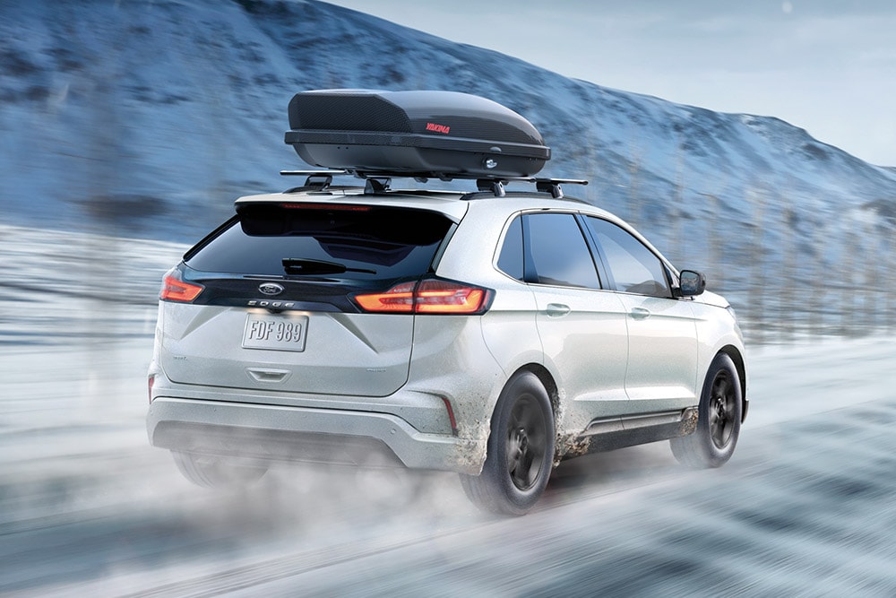  White Ford Edge with a roof box driving on a snowy mountain road, motion blur.