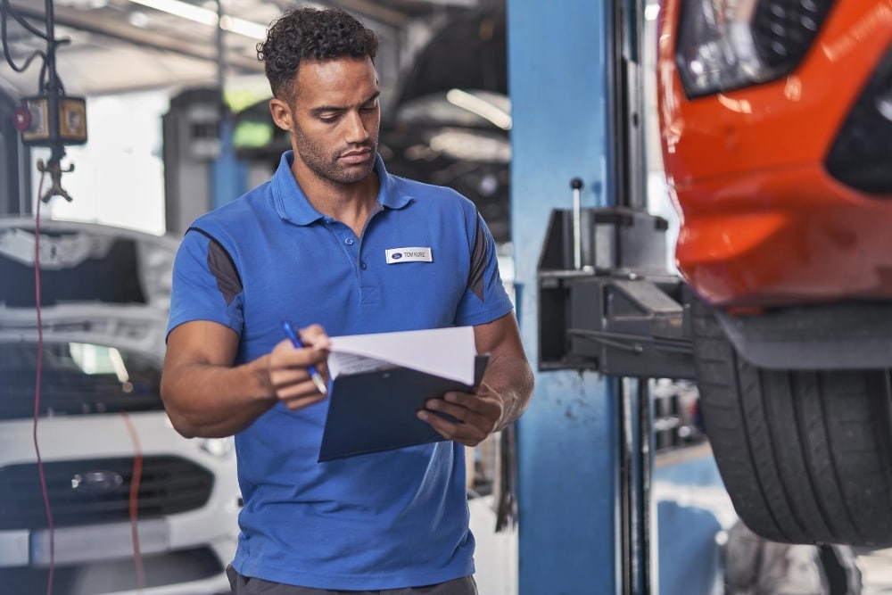 Tecnico addetto alla manutenzione Ford che controlla la cinghia di distribuzione e la pompa dell'acqua