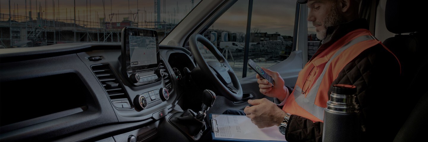 A Ford repairman using his phone while sitting in a Ford Transit